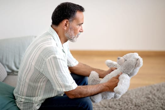 Depressed Senior Man Holding Toy Sitting On Couch At Home