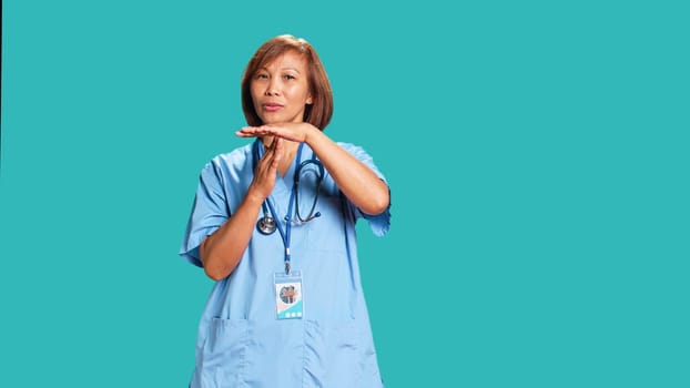 Assertive healthcare specialist asking for timeout while at work. Nurse doing pause hand sign gesturing, wishing for break from job shift, isolated over blue studio background