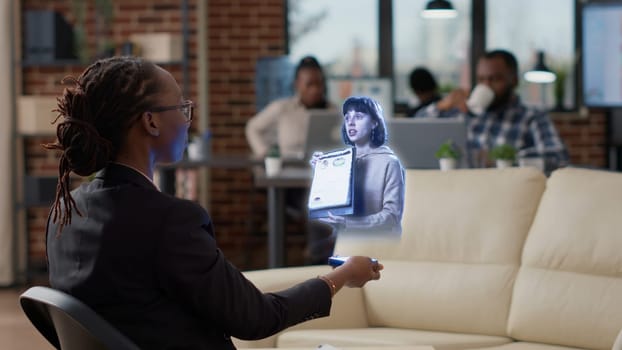 Team leader AR teleconference meeting, in high tech office talking with african american worker in . Businesswoman at workplace desk in online holographic videocall with manager