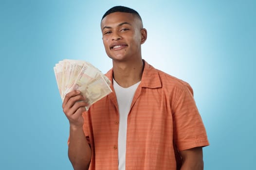 Young man, winner and money fan with success, bonus or winning in competition, college loan or cashback in studio. Portrait of student with cash, savings and scholarship funding on a blue background