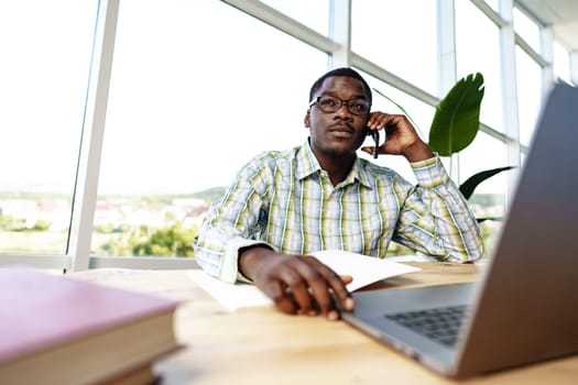 African man entrepreneur talking on cellphone and working on laptop at office
