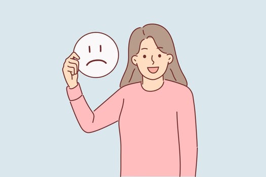 Happy woman holds sad emoticon calling to be optimist and have positive mood for achieve goals.