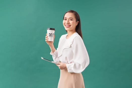 young woman holding digital tablet and paper cup isolated on green