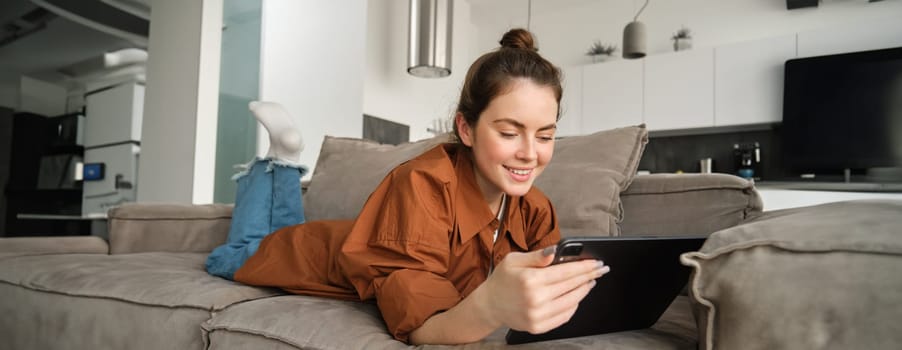 Weekend and lifestyle concept. Young woman lying on couch with digital tablet, scrolling social media, reading e-book or watching tv series on app