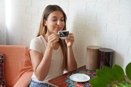 Coffee ads. Beautiful girl appreciates the smell of coffee at home. Young woman takes cappuccino in her apartment.