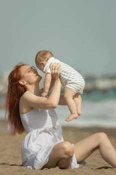 Happy mother and her little son resting on the seaside - raising the baby up