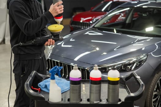 The master applies a special composition to the device for polishing the surface of the car body.
