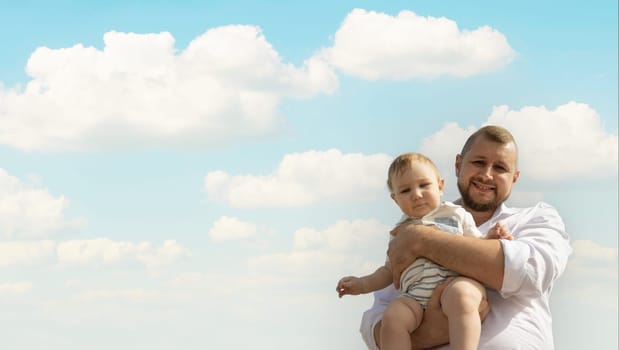 Happy father on vacation - man holding his little baby son on sky background