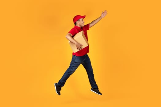 Arab deliveryman leaping with cardboard box over yellow studio background