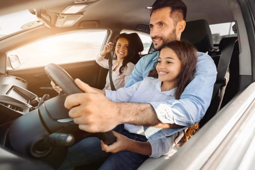 Smiling father drives with his cheerful daughter sitting beside, while mother looking at them and smiling, capturing warm family moment during a sunny day drive