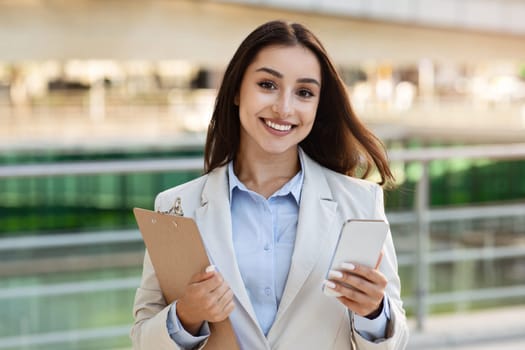 Smiling pretty confident young european lady in suit with clipboard, enjoy work