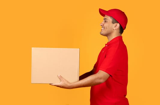 courier guy giving parcel carton box looking aside, yellow backdrop