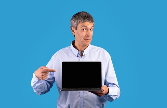 Mature businessman showing laptop pointing at empty monitor screen, studio