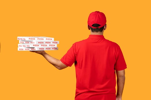 Rear view of courier holding pizza boxes over yellow backdrop