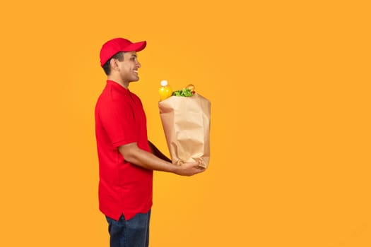 Mexican deliveryman carrying paper grocery bag with products, yellow background