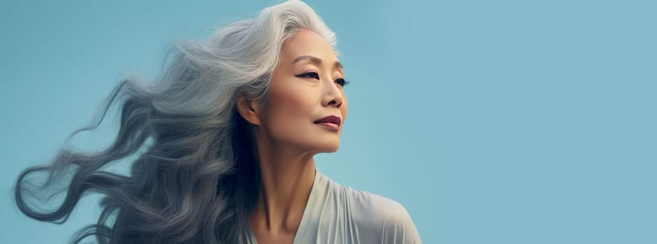 Smiling, elderly, gorgeous Asian woman with gray long hair and perfect skin, on a blue background, banner.