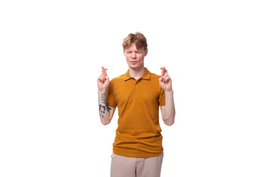 young smart red-haired man in a yellow t-shirt crossed his fingers in anticipation