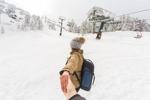 Follow me girl holding boyfriend hand in winter snow nature. Ski resort on the background