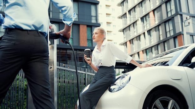 Progressive businessman and business woman unplug cable from electric car.