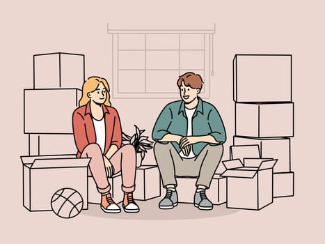 Couple sitting among boxes of belongings after moving into new house or apartment