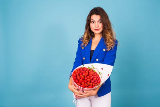 Young woman holding bouquet of strawberries on blue background.