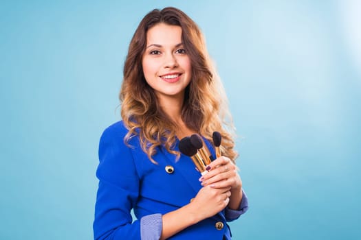 Young make-up artist with brushes on blue background