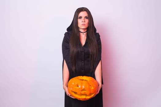 Young woman in Halloween witch costume in studio with yellow pumpkin.