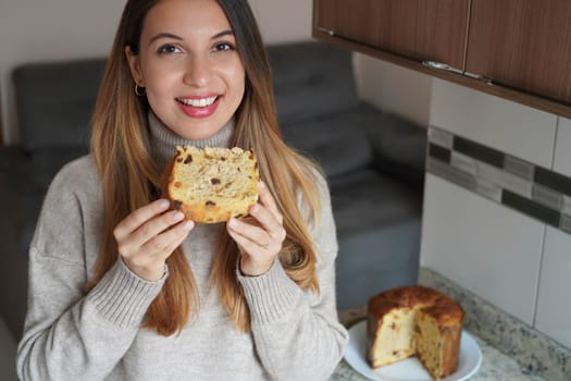 Portrait of beautiful woman holding a slice of Panettone traditional Italian cake for Christmas with raisins and candied fruits
