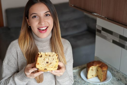 Portrait of happy beautiful woman holding a slice of Panettone traditional Italian cake for Christmas with raisins and candied fruits