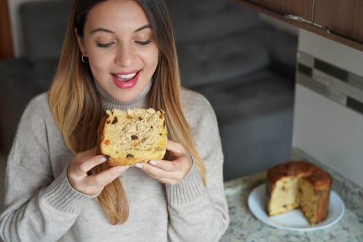 Close-up of happy young woman eating a slice of Panettone traditional Christamas cake with raisins and candied fruits indoor