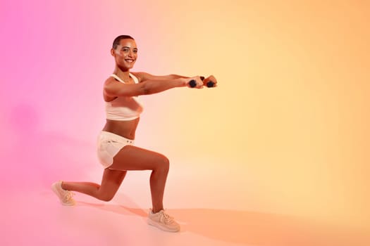 Smiling active young latin lady in sportswear doing arm exercises with dumbbells