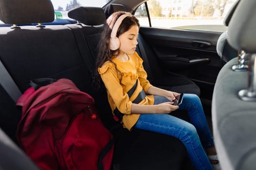Girl with headphones in car, engrossed in smartphone