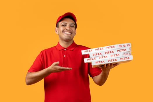Young Hispanic deliveryman in uniform holds pizza carton boxes, studio