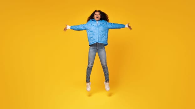 Shocked lady with open arms jumps on yellow background, full length