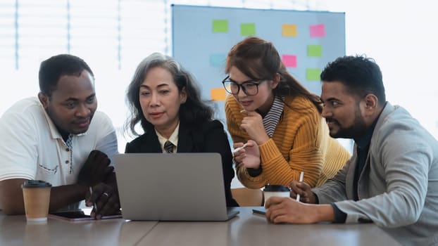 Happy senior old korean businesswoman discussing statistics concept on laptop with african american indian and asian male colleague working together workplace, analyzing electronic documents