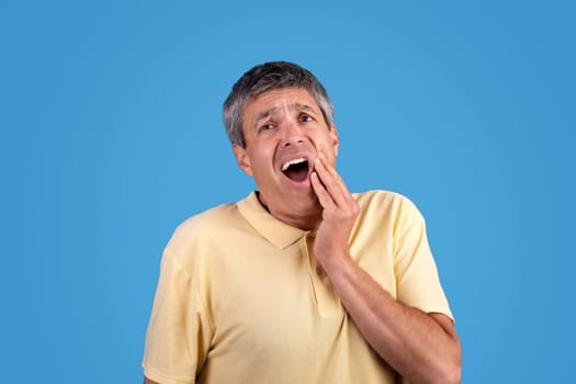 Older man suffering from tooth pain over blue backdrop