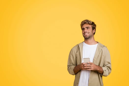 Young European man with cellphone, looking at empty space on yellow