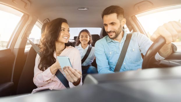 Family enjoying a car ride with mother holding a phone and child smiling in the back