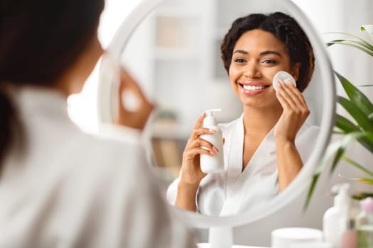 Skincare Routine. Black woman using makeup remover and cotton pad at home