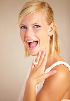 Woman, excited and engagement ring in studio portrait with smile for proposal, wedding or commitment by background. Girl, model and jewelry for marriage, diamond and metal for celebration at ceremony