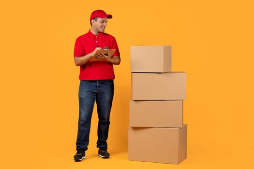 Arab courier with clipboard near stack of cardboard boxes, studio