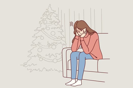 Woman is sitting on sofa near christmas tree and is sad because of loneliness and lack of friends