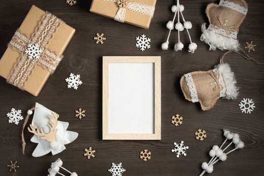 An empty frame on a wooden table surrounded by Christmas gifts and ornaments made of natural materials. A mockup for greeting cards and advertisements