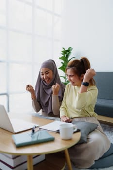 Muslim undergraduate students and Asian women express their joy after completing online study using a computer.