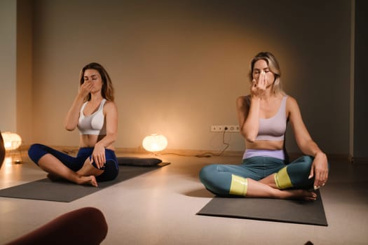 a couple of women performing breathing exercises while sitting on a yoga mat. yoga meditation in the fitness room