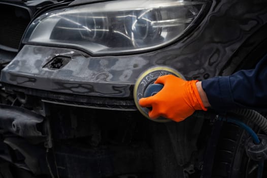 A mechanic sands the putty on a car body with a machine. Repair after an accident.
