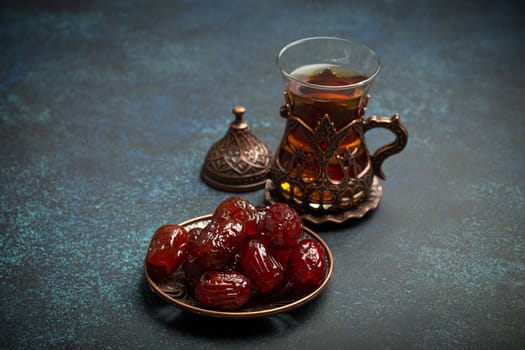 Breaking fasting with dried dates during Ramadan Kareem, Iftar meal with dates and Arab tea in traditional glass, angle view on rustic blue background. Muslim feast