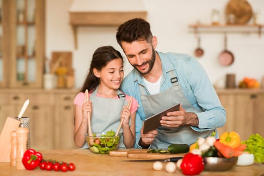 Father and daughter looking at tablet while cooking in kitchen