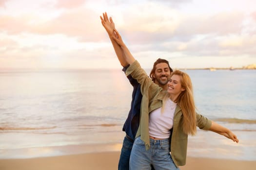 Young romantic couple on beach acting like they're flying, arms outstretched