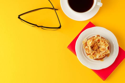 Tartlet with almond petals and cup of coffee on yellow background